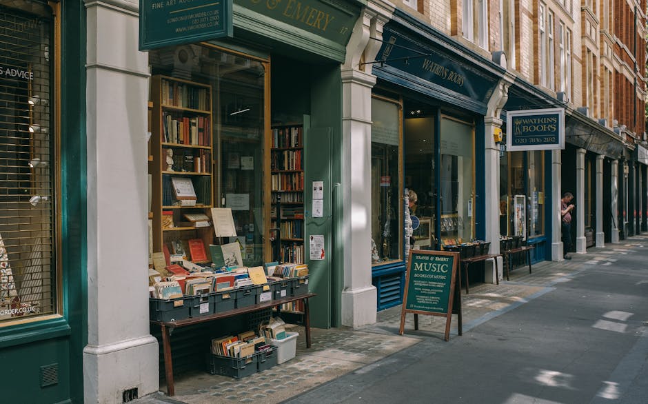 A floral arrangement featuring a vibrant bouquet of fresh flowers, including pink roses, white lilies, purple and yellow blooms with green foliage, is held by a person standing outside a bookshop on a