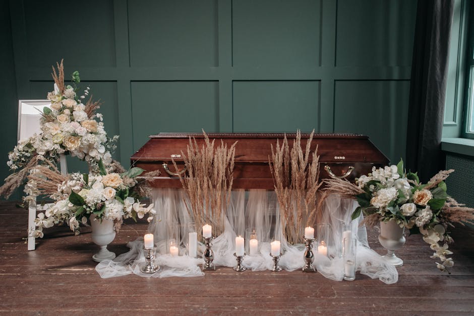A floral arrangement placed on a polished wooden surface in front of a green paneled wall, featuring two large white vases filled with cream and white roses, pale pink peonies, and white hydrangeas, a