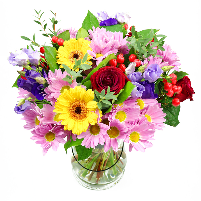 A vibrant mixed bouquet fills the frame, its many colours and textures carefully composed in a clear glass vase that sits on an invisible surface against a pure white backdrop. The central eye is drawn first to the rich red roses, their velvety petals curling in tight, romantic spirals, suggesting classic affection and a touch of drama, as if they were chosen to echo the literary history of Bloomsbury. Surrounding them, two bold yellow gerbera daisies stand slightly taller, their broad, daisy-like petals radiating out from deep brown-orange centres, adding a burst of sunshine that feels as welcoming as stepping into one of the area's leafy squares. Encircling these focal flowers, generous clusters of soft pink and lavender daisy or chrysanthemum blooms create a cushion of colour, each head made up of numerous fine petals with pale yellow centres, adding volume and a gentle, cloud-like softness to the overall silhouette. Threaded through this pastel halo are slender stems of lisianthus in shades of purple and lilac, their graceful, bell-shaped flowers and ruffled edges giving the design a sense of movement and subtle elegance. Dotted between petals, bright red hypericum berries add pops of glossy colour and a pleasing roundness that contrasts with the layered petals, like tiny treasures hidden in a garden border along nearby Woburn Walk. The bouquet is framed with varied greenery-broad, dark green leaves that anchor the composition and lighter, more delicate sprigs that reach outward-creating a feeling of freshness and natural abundance. Visible through the transparent vase, neatly angled stems rest in clear water, highlighting the skill and care of the florist who has balanced structure with softness. The overall impression is of joyful sophistication and heartfelt warmth, ideal for birthdays, thank-you gifts, or quiet celebrations at home anywhere in Bloomsbury.